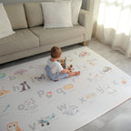 Child sitting on a colorful play mat with letters and illustrations in a living room.