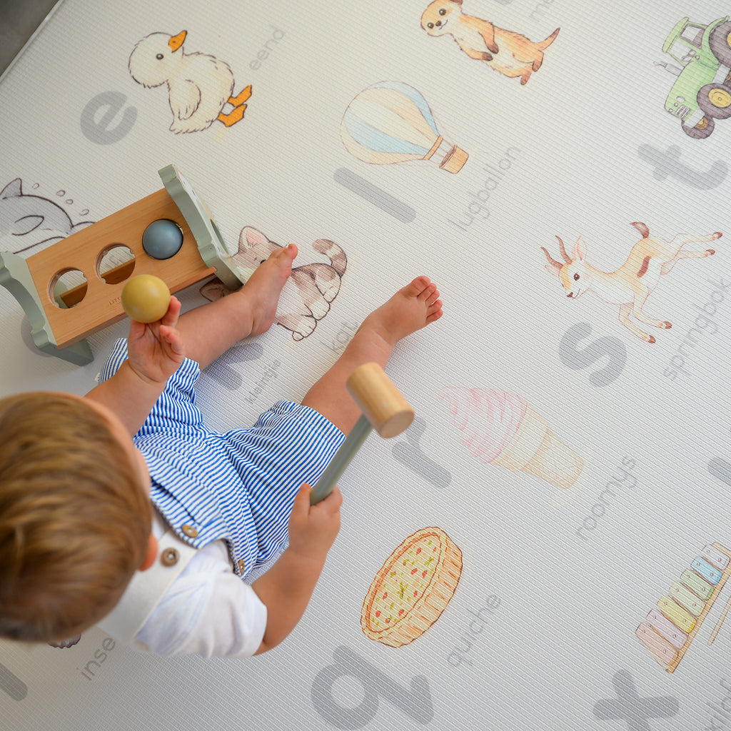 Child playing with wooden toys on a play mat with illustrations and letters.