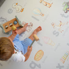 Child playing with wooden toys on a play mat with illustrations and letters.