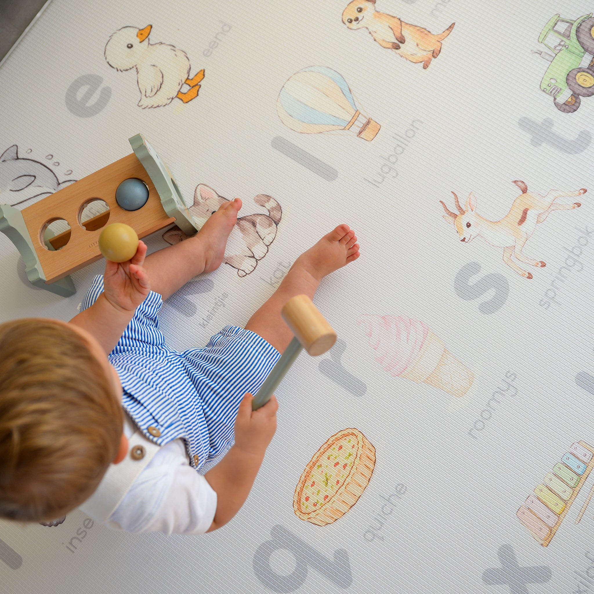 Child playing with wooden toys on a play mat with illustrations and letters.