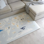 World map play mat with animal illustrations on a light-colored floor next to a beige sofa.