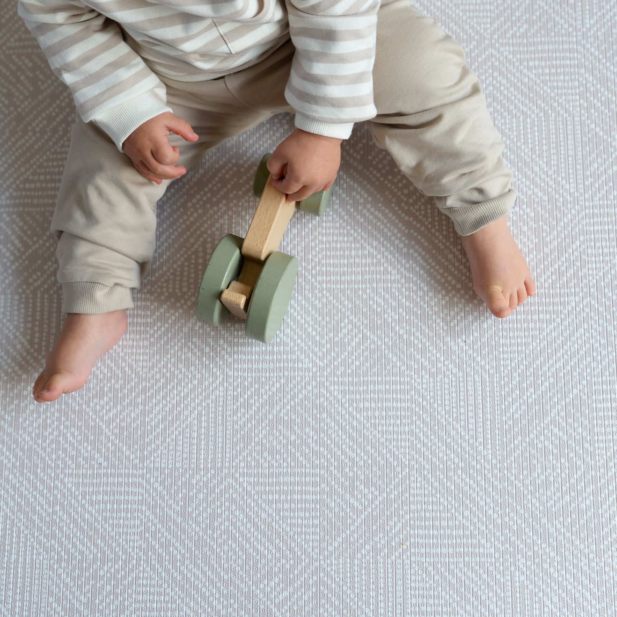 Child playing with a wooden toy on a textured play mat