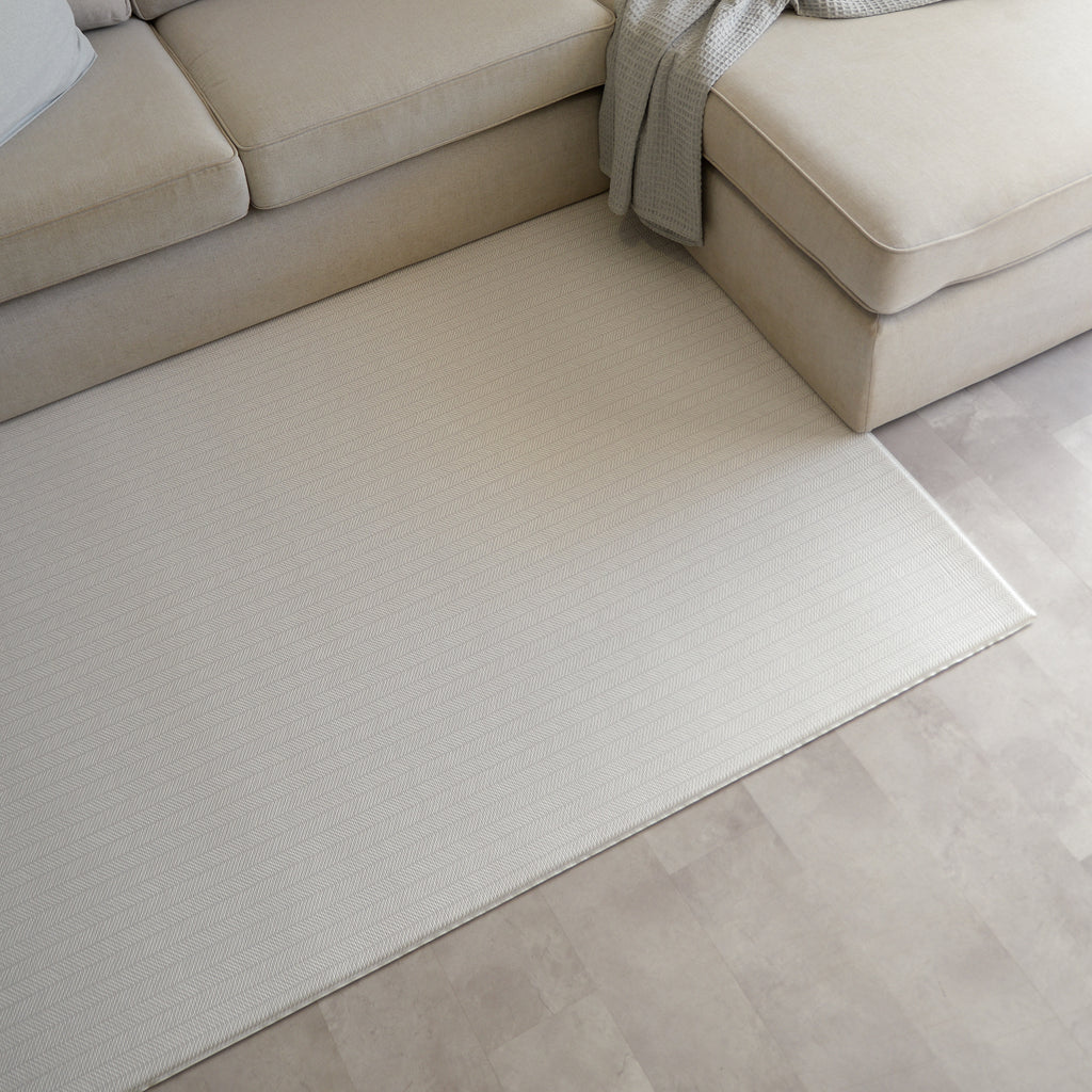 Sage herringbone patterned play mat on a tiled floor next to a beige sectional sofa