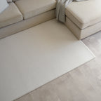 Sage herringbone patterned play mat on a tiled floor next to a beige sectional sofa
