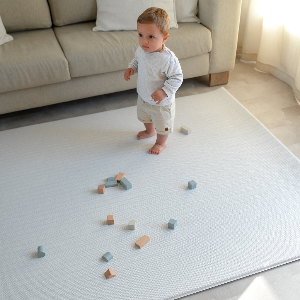 Child playing with wooden blocks on a soft play mat in a living room.