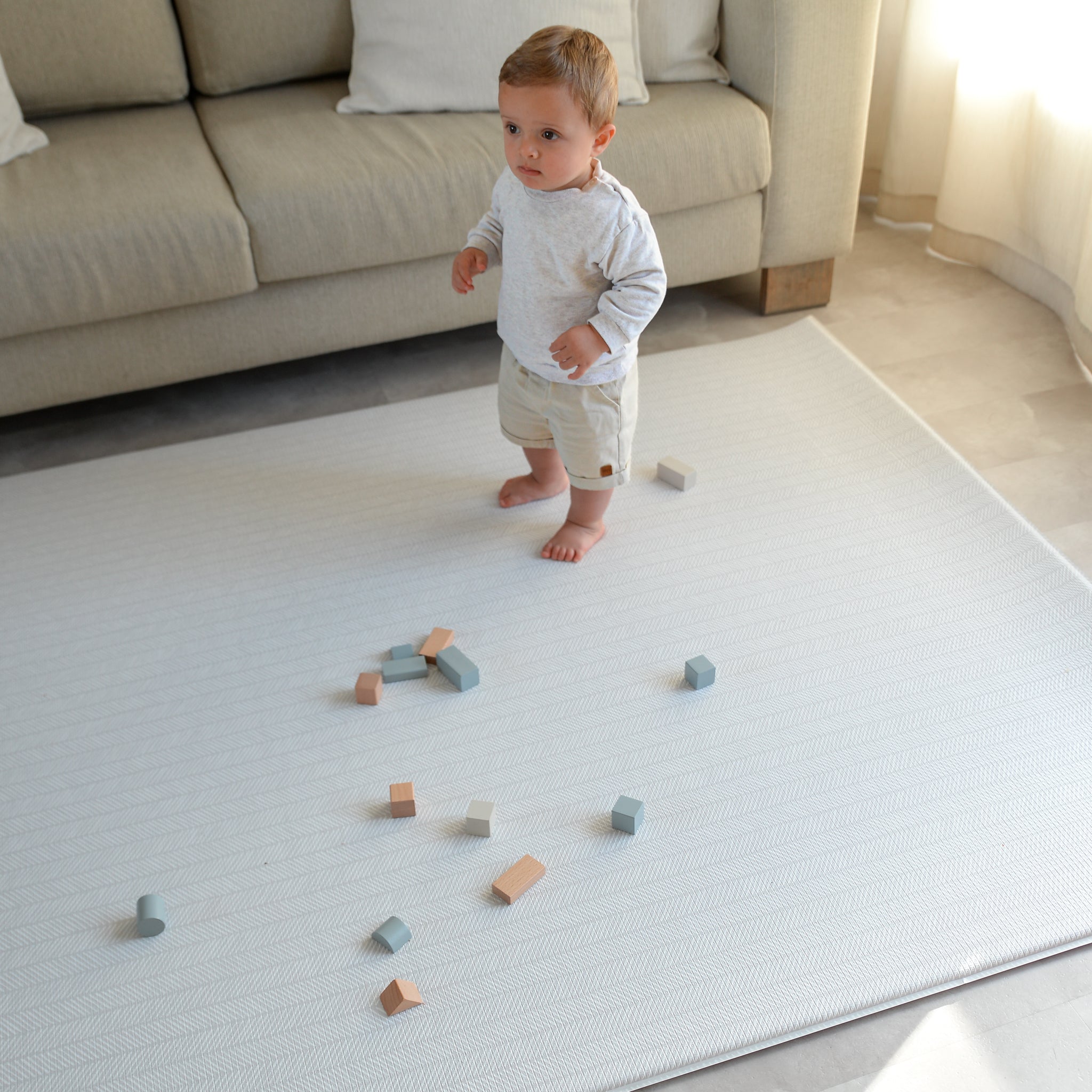 Child playing with wooden blocks on a soft play mat in a living room.