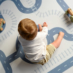 Child playing on a road-themed play mat with toy cars.