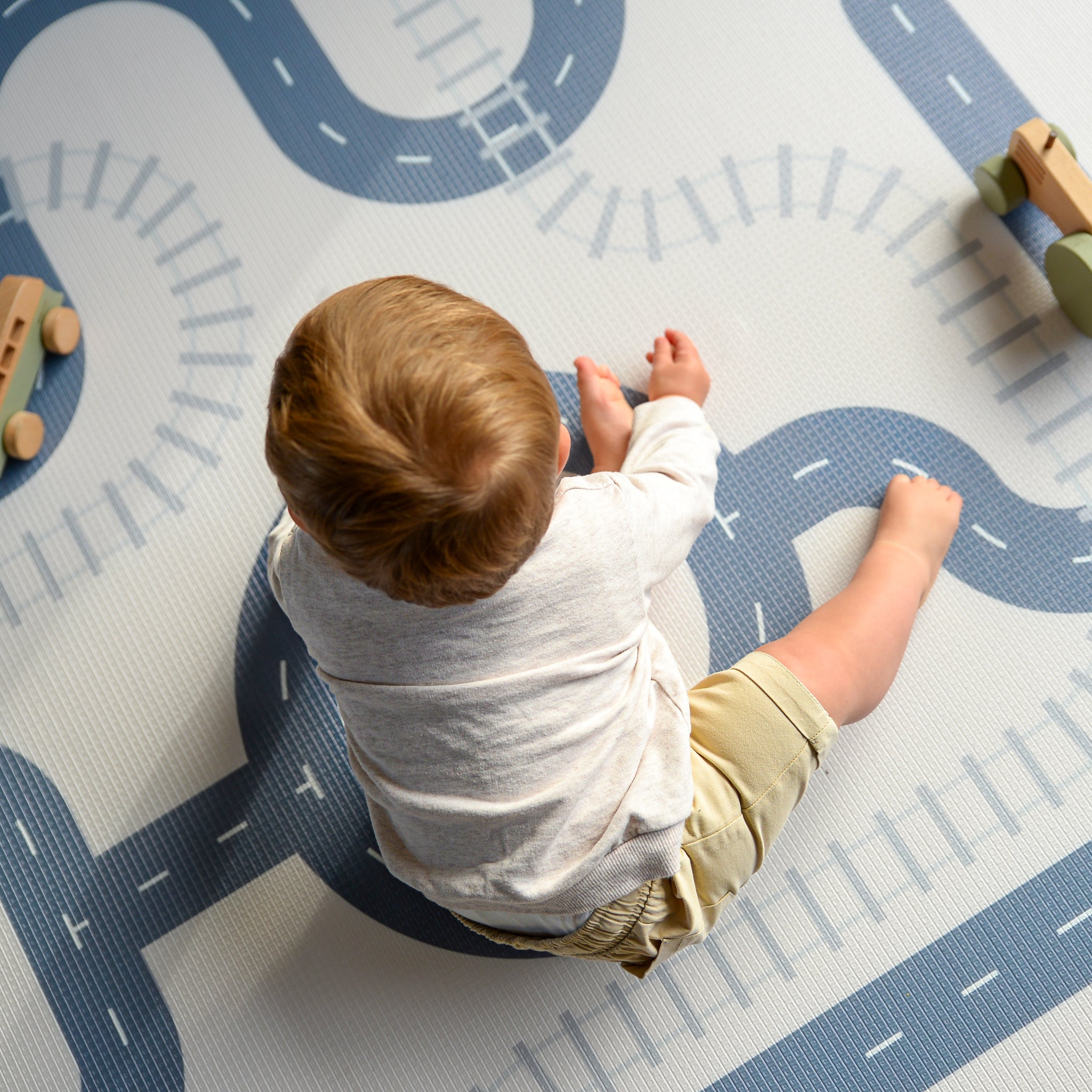 Child playing on a road-themed play mat with toy cars.
