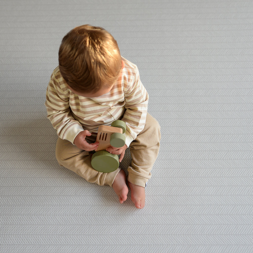 Child playing with wooden toys on a herringbone patterned play mat