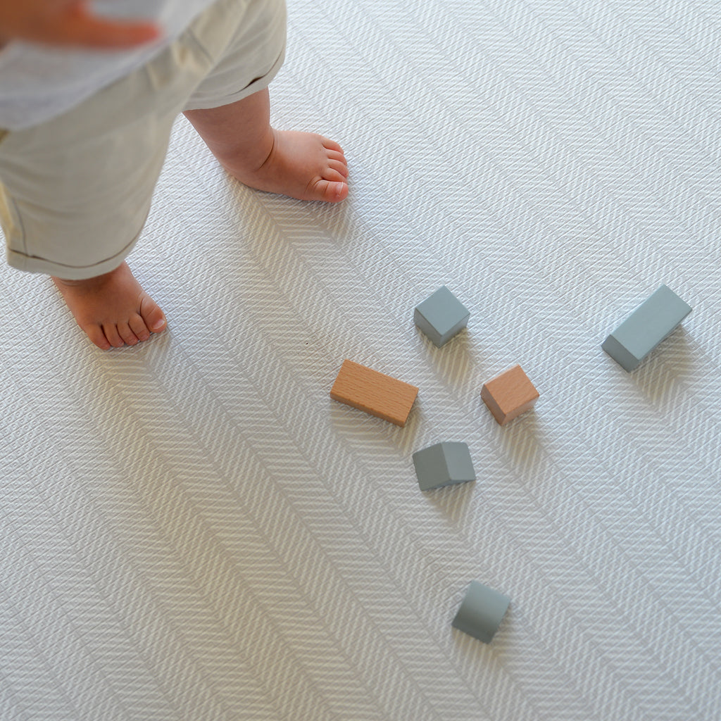 Child's feet near geometric blocks on a herringbone pattern play mat
