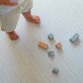 Child's feet near geometric blocks on a herringbone pattern play mat
