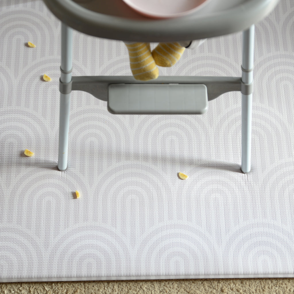 Child's high chair on a patterned play mat with scattered food