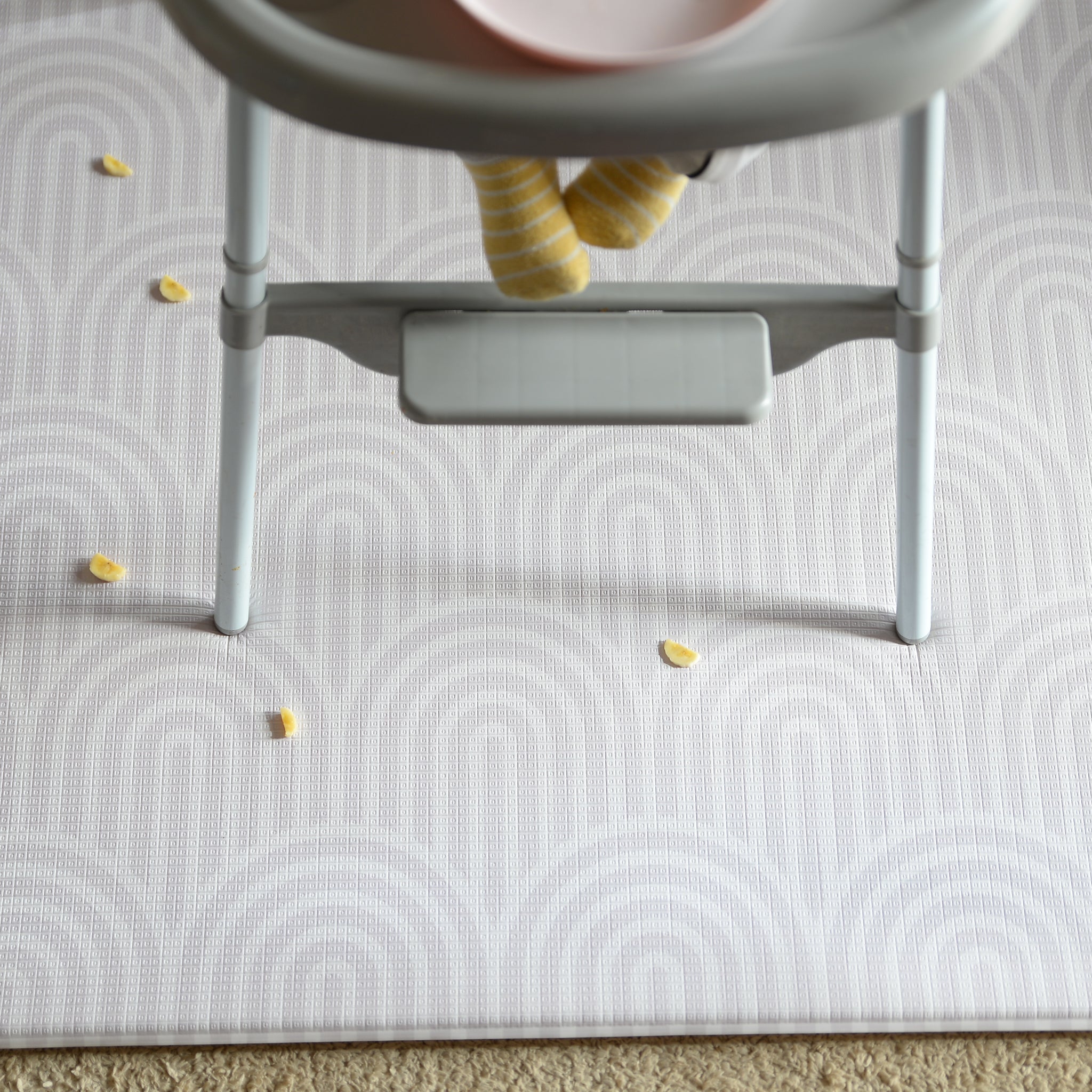 Child's high chair on a patterned play mat with scattered food