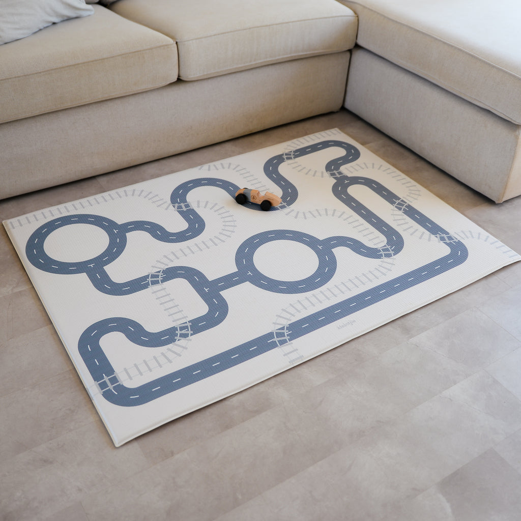 Play mat with a race track design on a beige floor next to a beige sofa.
