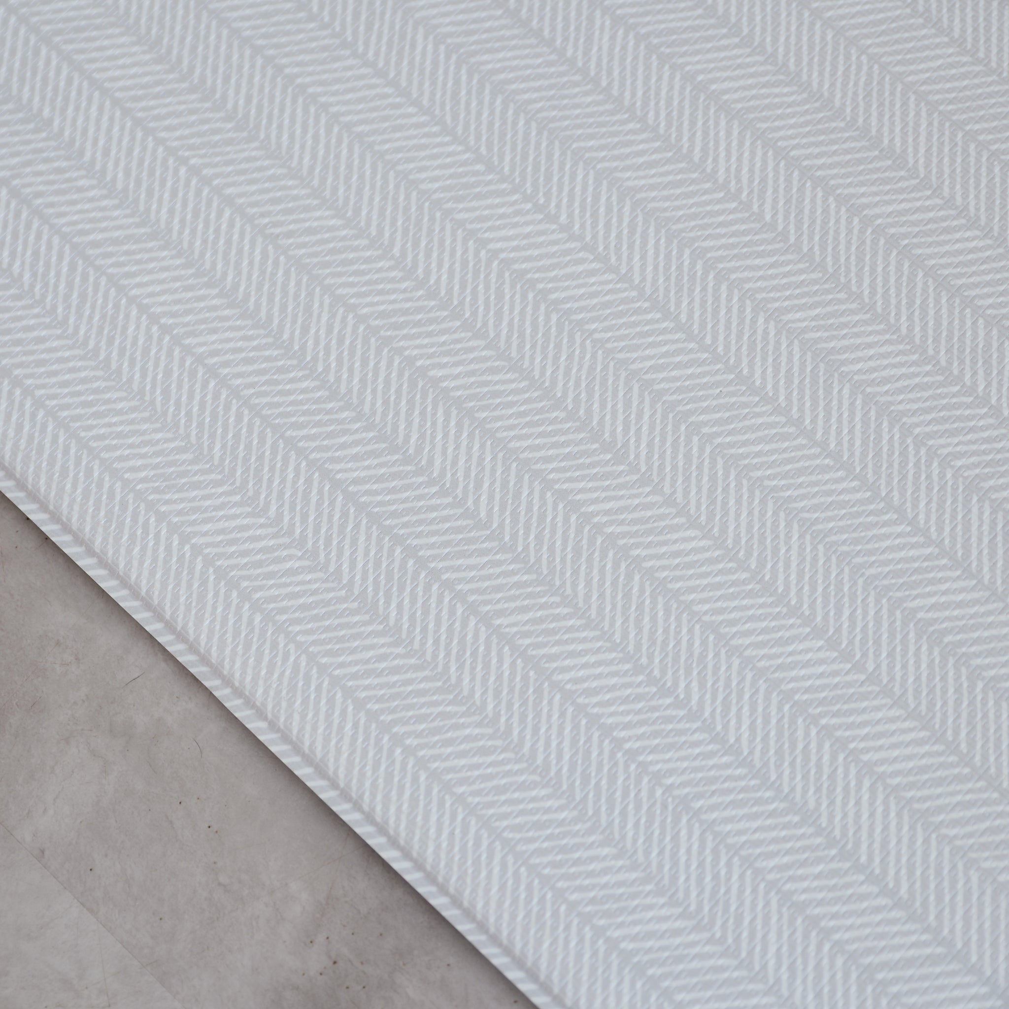 Sage play mat with a herringbone pattern on a concrete floor.