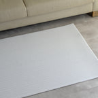A modern play mat with a sage herringbone pattern on a gray floor in a room with a beige sofa.