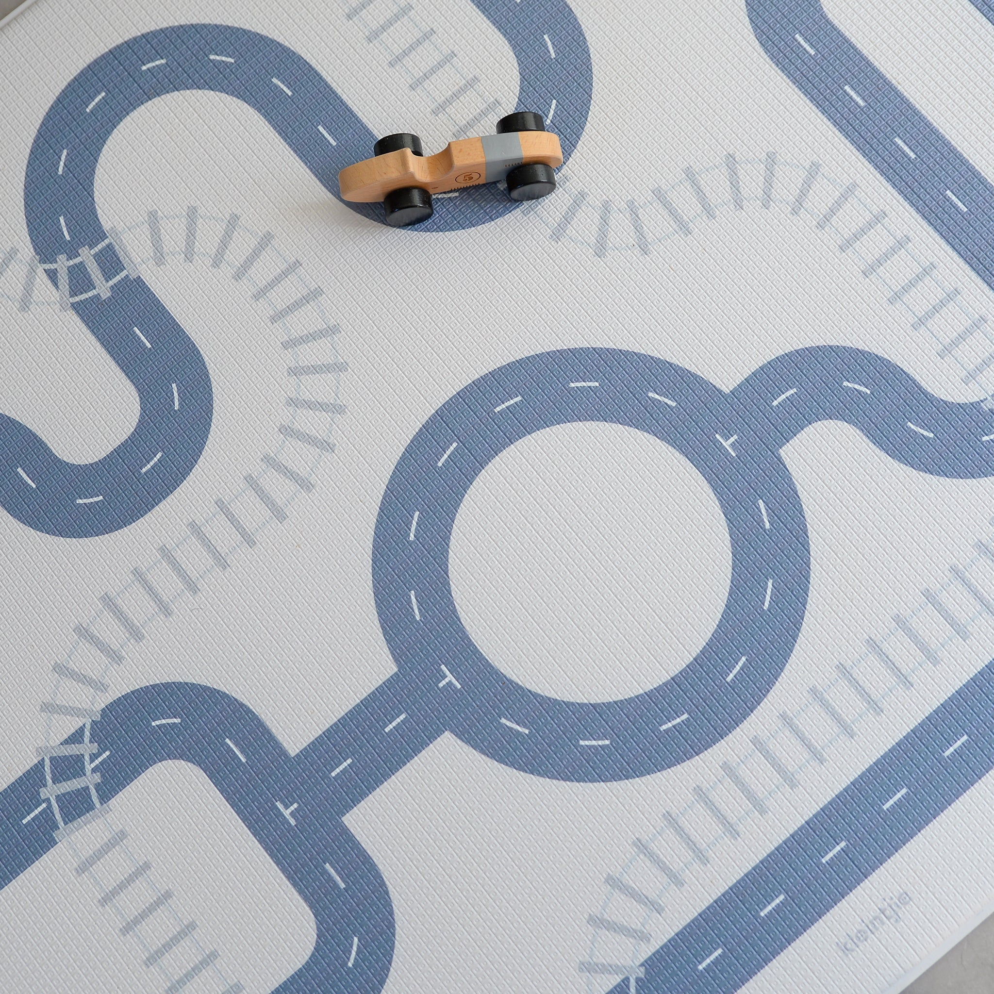 Play mat with road design and toy cars on a light gray background