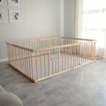Wooden playpen and play mat in a room with light gray flooring and white walls.