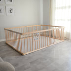 Wooden playpen and play mat in a room with light gray flooring and white walls.