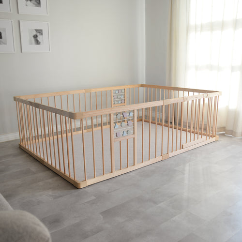 Wooden playpen and play mat in a room with light gray flooring and white walls.