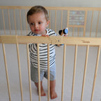 Child standing in a wooden baby playpen with built-in toys in a room.
