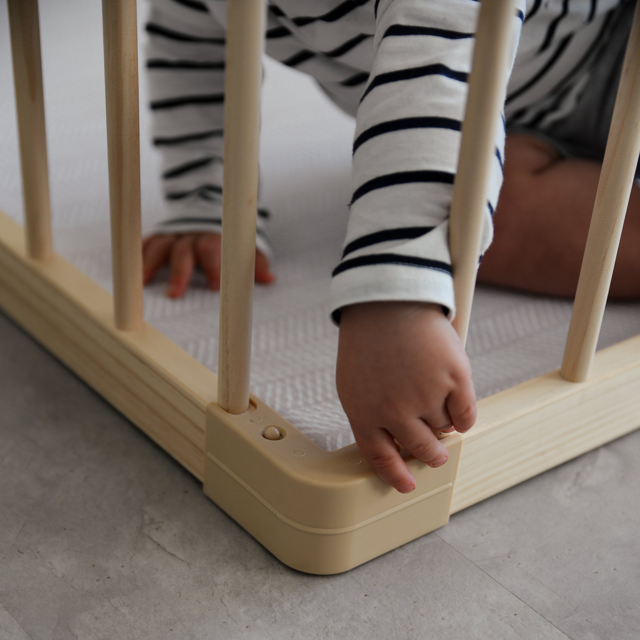 Child's hand reaching through a baby playpen with striped shirt on