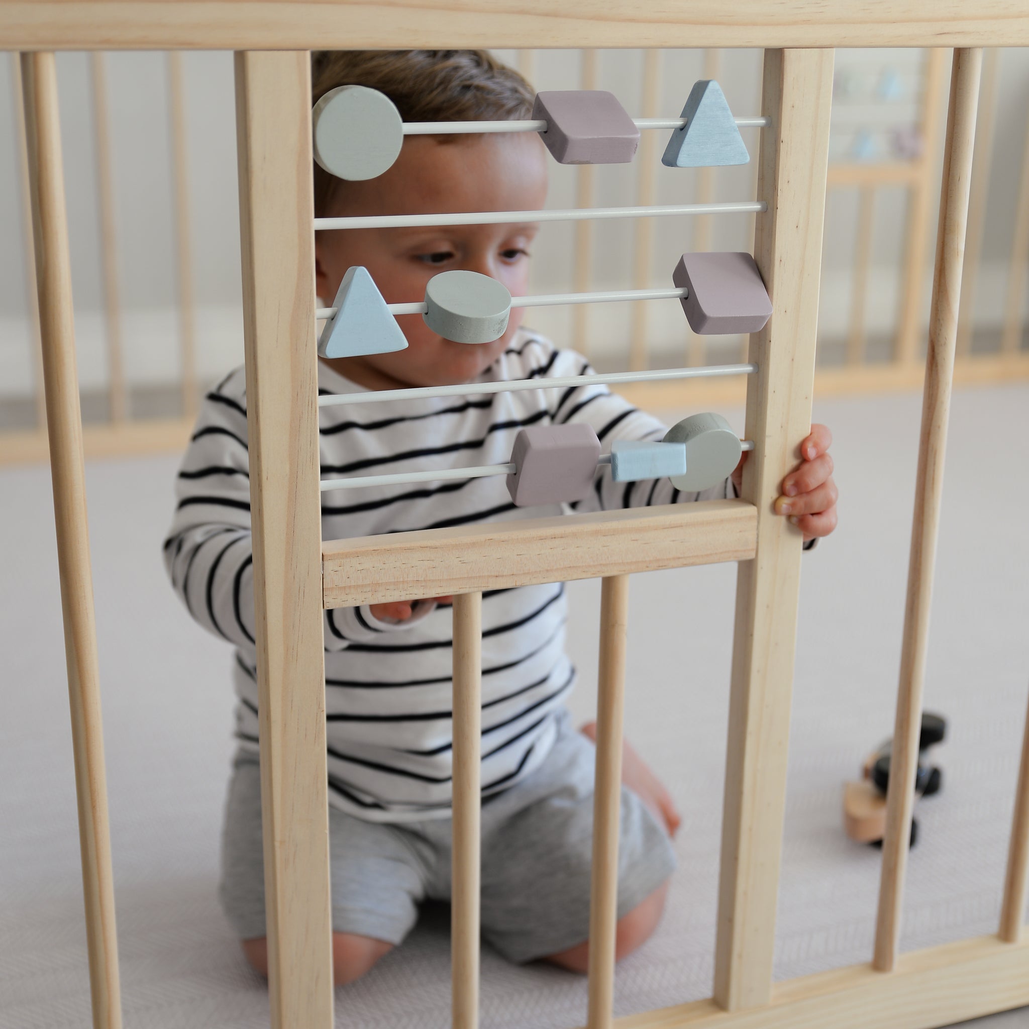 Child playing with geometric shapes in a wooden playpen