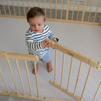Child standing on a play mat in a wooden baby playpen in a room
