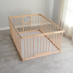 Wooden baby playpen with a play mat on a light wooden floor.
