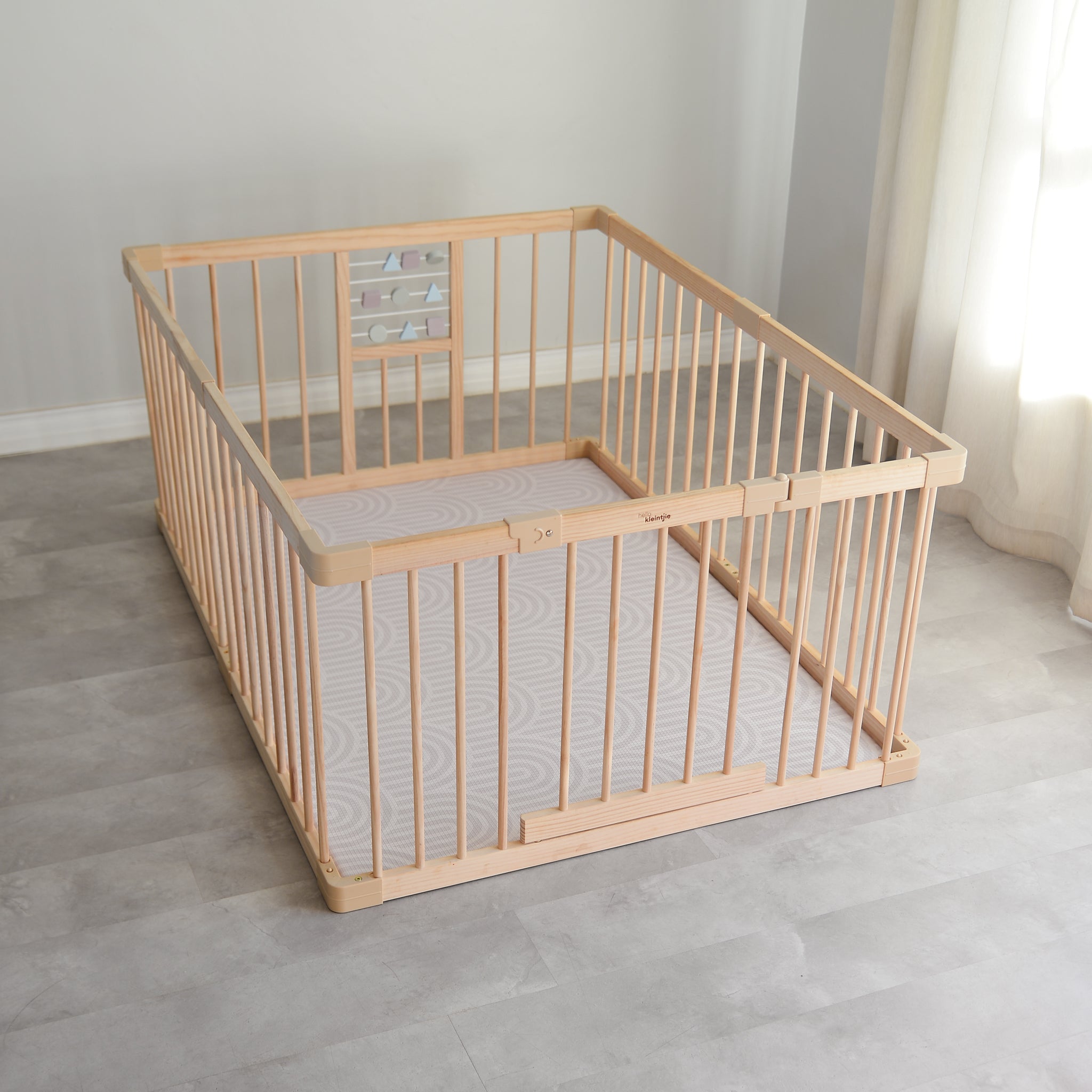 Wooden baby playpen with a play mat on a light wooden floor.