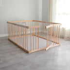 Wooden baby playpen and play mat in a minimalistic room with light gray flooring and white walls.