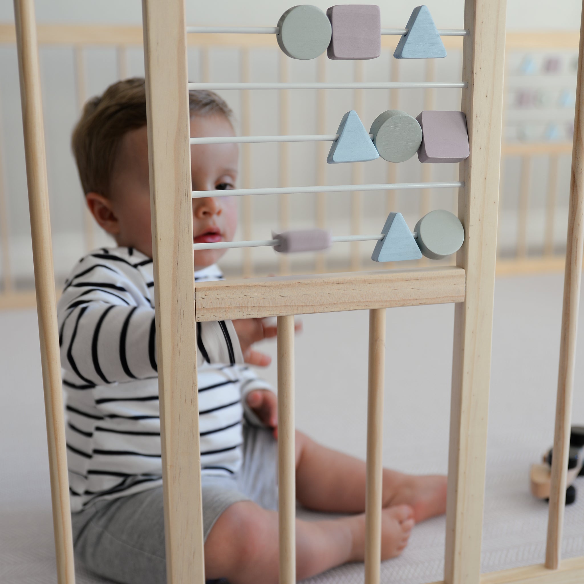 Child playing with a wooden geometric toys in a wooden playpen