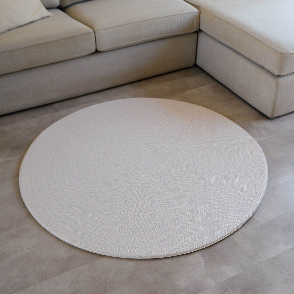 Beige play mat with a herringbone pattern on a concrete floor.